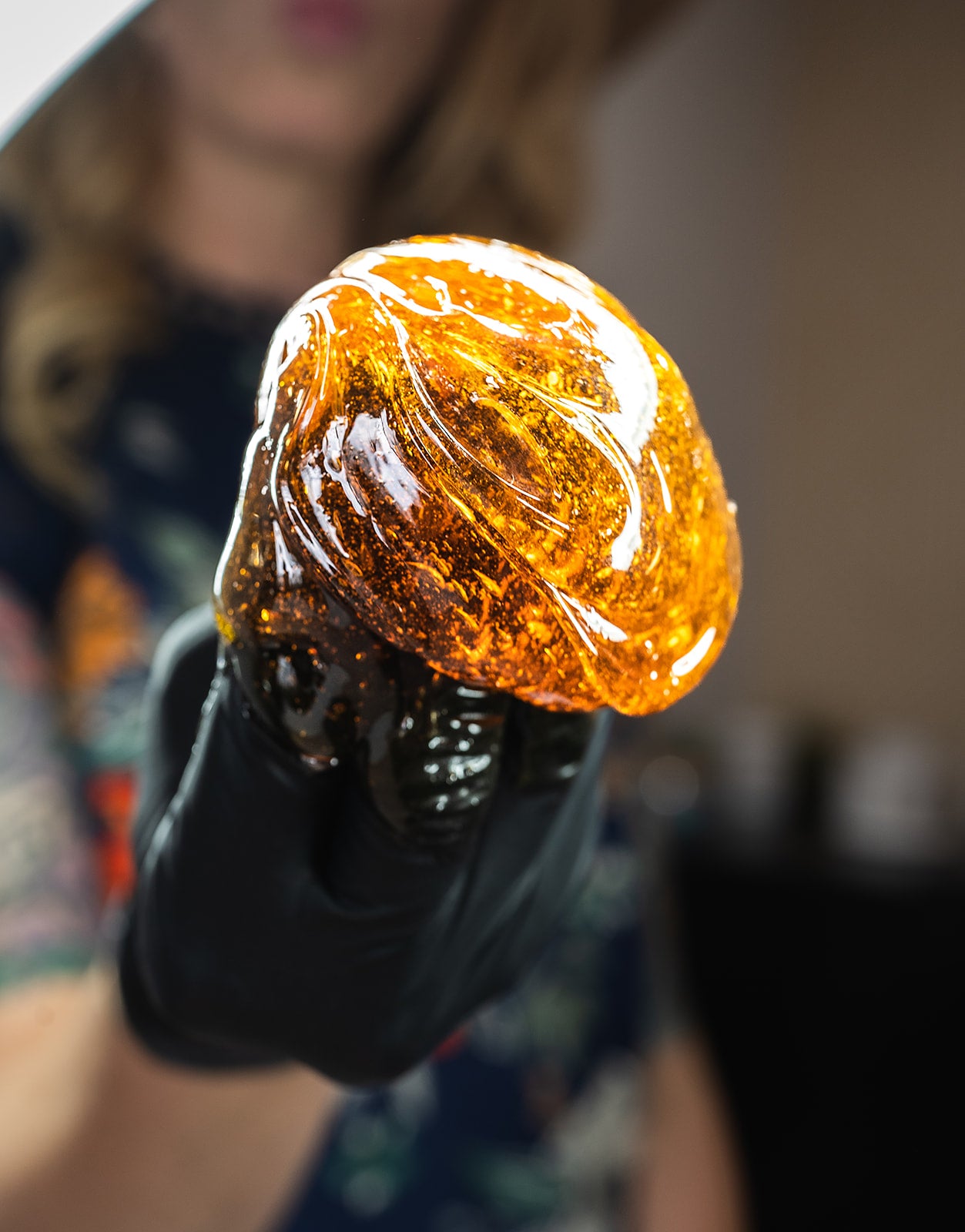 Amber-colored sugar wax held by a person wearing a black glove against a blurred background