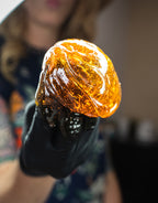 Amber-colored sugar wax held by a person wearing a black glove against a blurred background