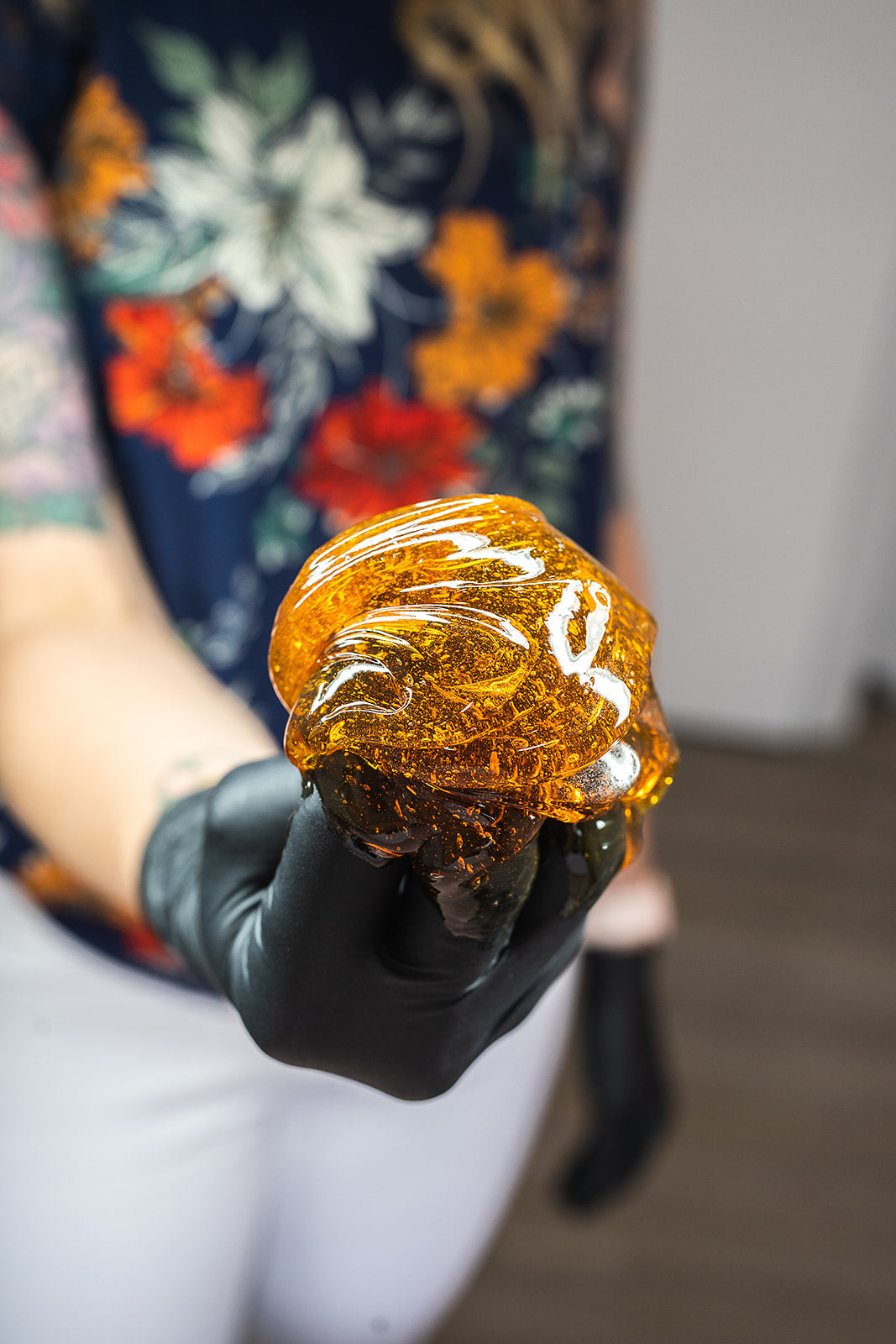 nitrile gloves holds up a glossy, translucent amber-colored paste