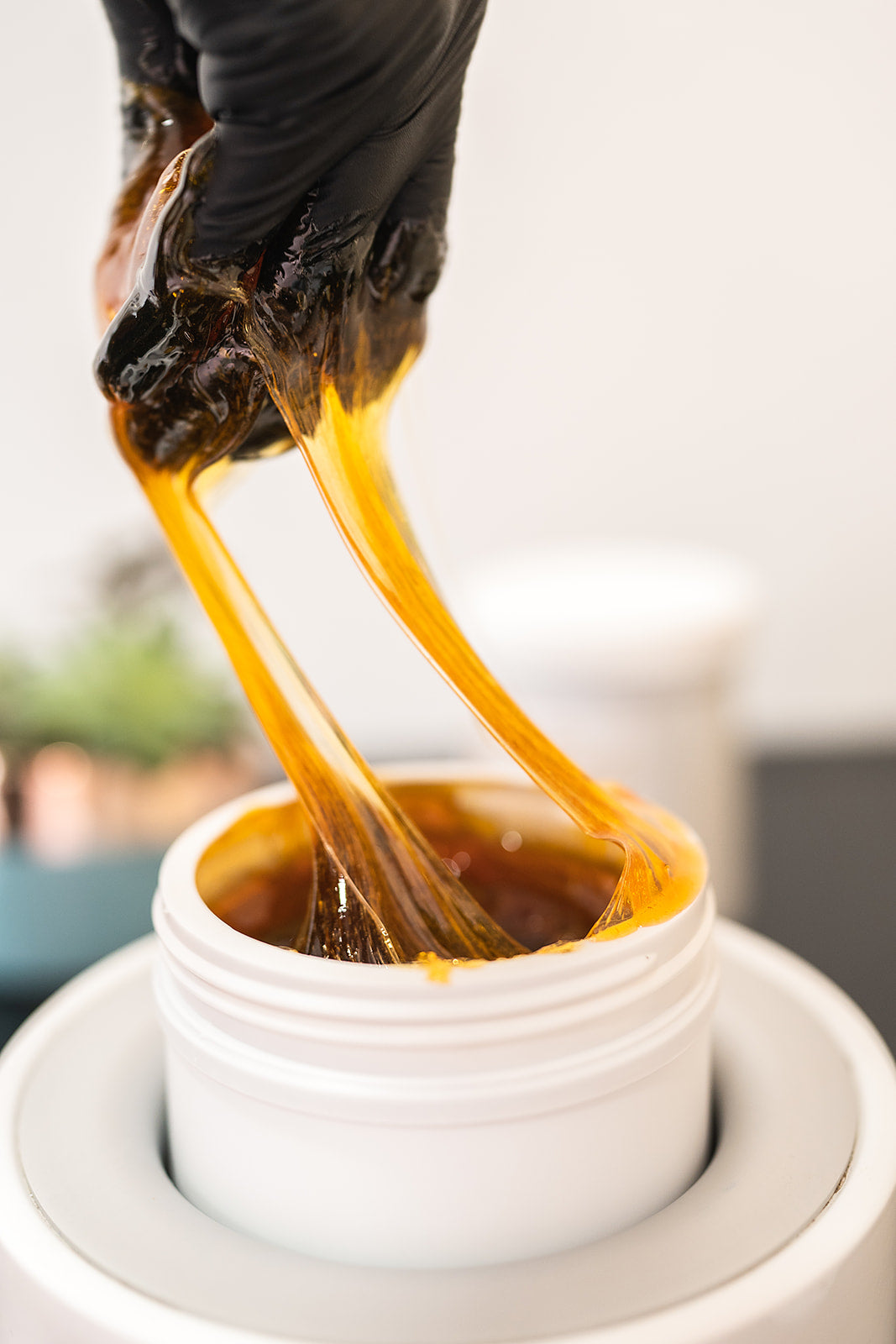 Hand wearing a black glove pulling amber-colored paste/wax from a warmer